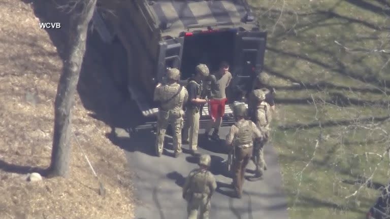 Esta imagen tomada de un video proporcionado por WCVB-TV, muestra a Jack Teixeira, en camiseta y pantalones cortos, siendo puesto bajo custodia por agentes tácticos armados el jueves 13 de abril de 2023, en Dighton, Massachusetts 