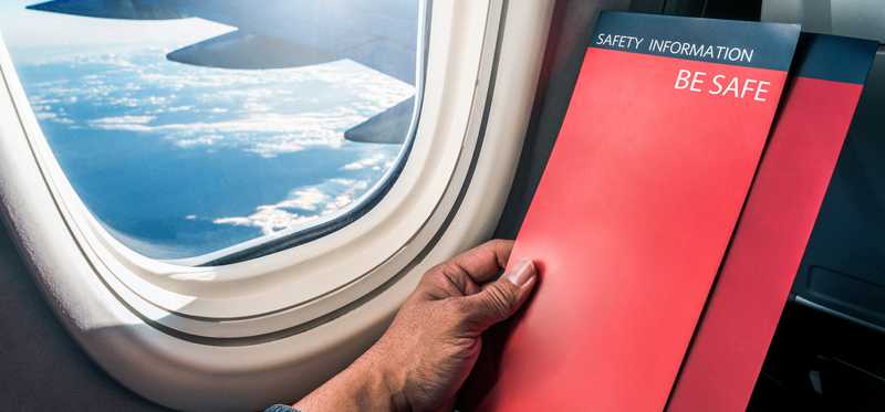 Passenger reading plane safety manual as he sits in a window seat.