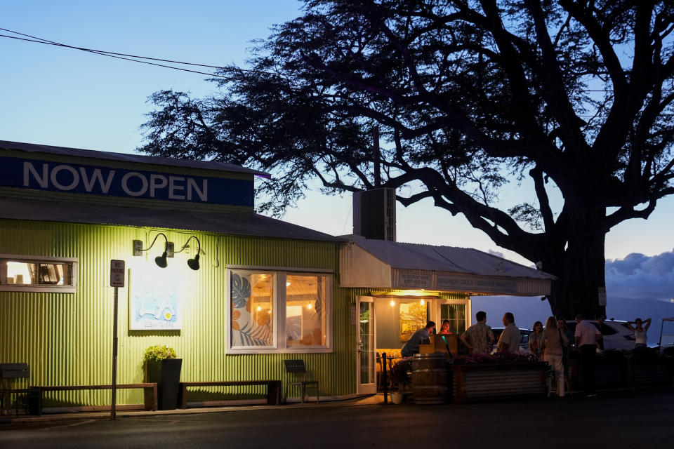 A "Now Open" sign is displayed as people eat at the Mala Ocean Tavern, a business on Front Street that survived the wildfire, Friday, July 5, 2024, in Lahaina, Hawaii. (AP Photo/Lindsey Wasson)