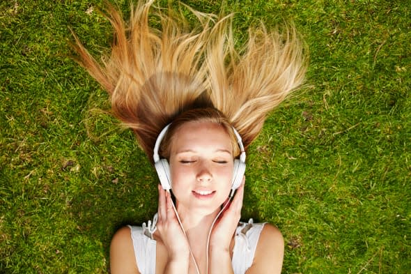 Girl listening to music streaming with headphones in summer on a meadow