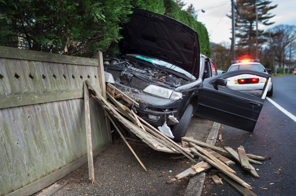 Car crashed into a wooden fence with a police car behind