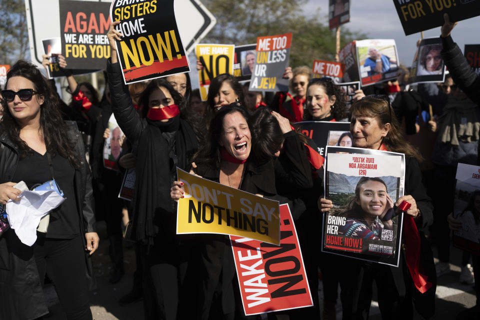 Relatives and supporters of the Israeli hostages held in the Gaza Strip by the Hamas militant group attend a march calling for their release near Kibbutz Urim, southern Israel, Friday, Jan. 12, 2024. Seeking to bring attention to the abuse of female hostages remaining in the Strip, they bound themselves with red tape, chanted "bring our sisters home!," and marched behind a woman who writhed inside a cage. (AP Photo/Ohad Zwigenberg)