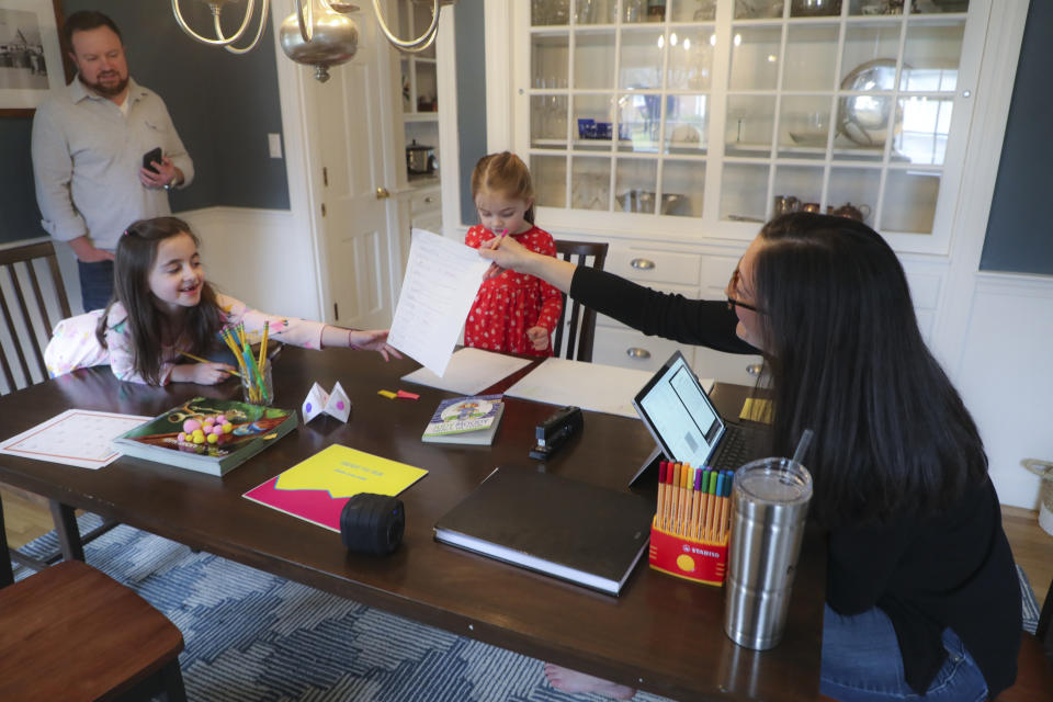 Sarah Yunits checks her daugher Ada's homework while Cora waits her turn as dad Conor Yunits is on a work conference call at their home in Brockton on March 19, 2020. (Photo by Matthew J. Lee/The Boston Globe via Getty Images)                             