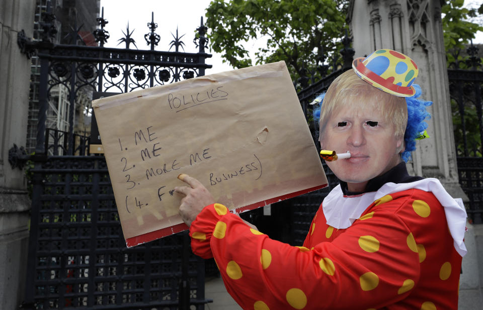 A demonstrator in a Boris Johnson mask poses with a banner outside the Houses of Parliament in London, Thursday, June 20, 2019. The contest to become Britain's next prime minister is down to its final three candidates, with Environment Secretary Michael Gove and Foreign Secretary Jeremy Hunt chasing front-runner Boris Johnson for a spot in a deciding runoff. (AP Photo/Kirsty Wigglesworth)