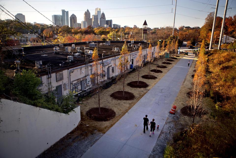 FILE- In this Nov. 20, 2012 file photo, a couple walks along the Atlanta BeltLine as the midtown skyline stands in the background in Atlanta. The Atlanta BeltLine is an urban redevelopment project that aims to turn an old 22-mile railroad corridor that rings the city’s in-town neighborhoods into a network of trails, parks, affordable housing and, eventually, transit. So far, only the 2.2-mile Eastside Trail has opened, with skyline views and regularly changing public art installations providing added scenery for those who walk, bike and jog along the path. (AP Photo/David Goldman, File)