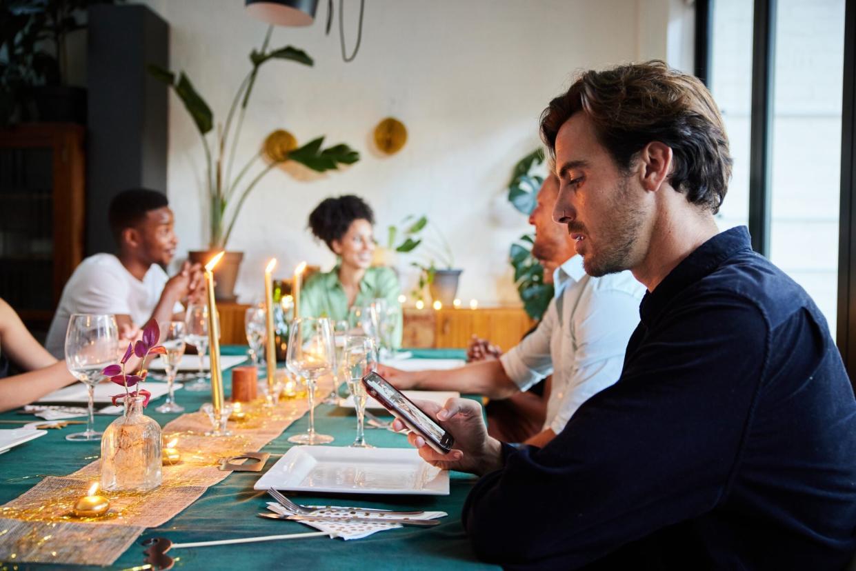 Young man reading a text message during a dinner party with friends