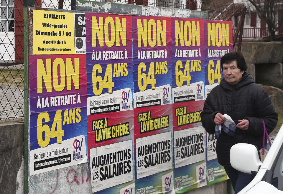 A woman walks past "No retirement at 64" posters in Saint Pee sur Nivelle, southwestern France, Monday, March 6, 2023. Unions are threatening to shut France's economy down this week in what they hope is their toughest riposte yet to President Emmanuel Macron's plan to raise the retirement age. (AP Photo/Bob Edme)