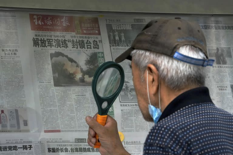 Un hombre usa una lupa para leer un periódico que informa sobre ejercicios militares de China alrededor de Taiwán, en Pekín, el 7 de agosto de 2022.
