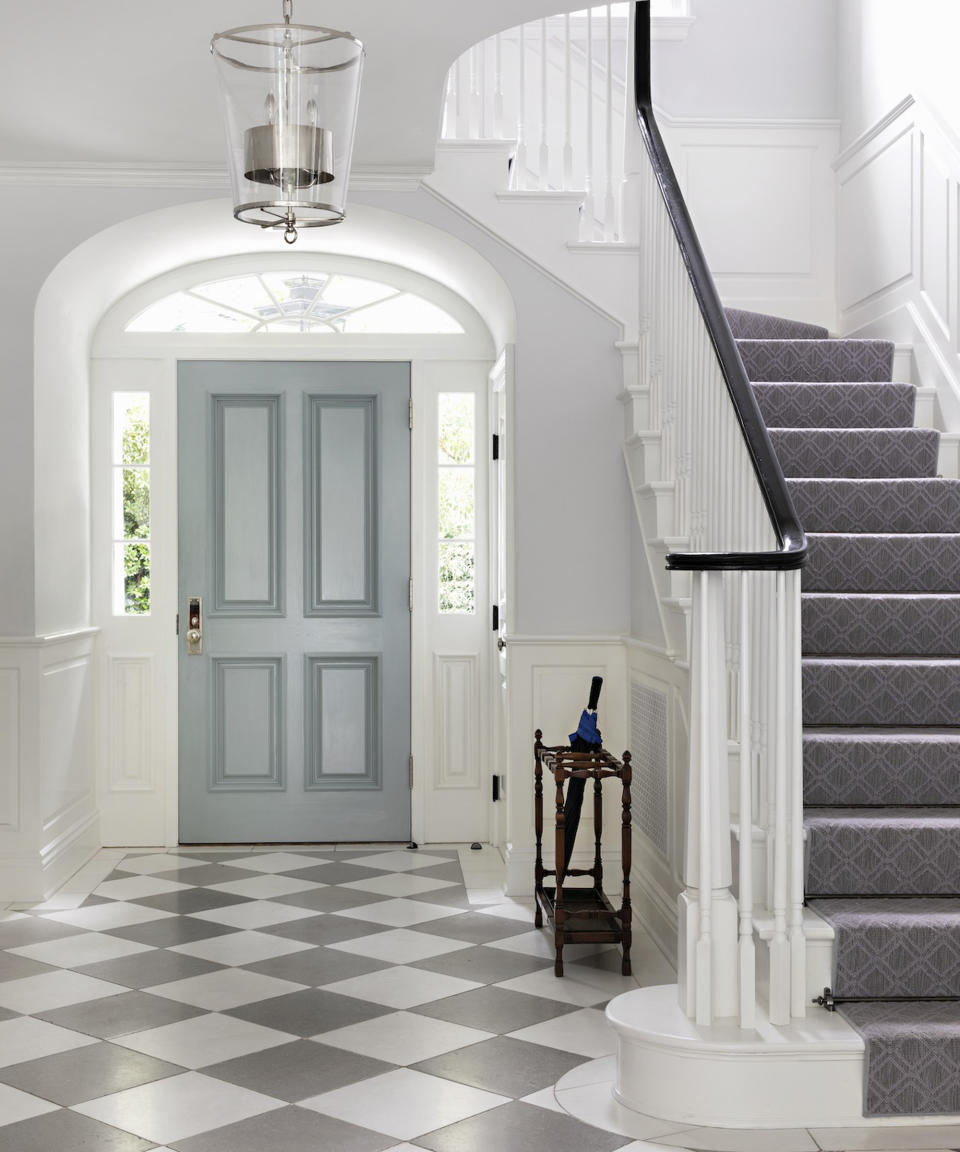 Gay and white checkered floor tiles and a sweeping white staircase.