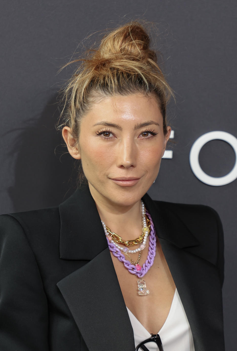 Dichen Lachman in a black blazer over a white top, with layered necklaces, attending an event