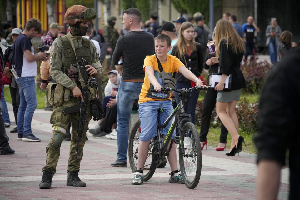 FILE - A Russian serviceman stands guard as local civilians walk in the center of Melitopol, Zaporizhzhia region, in territory under Russian military control, southeastern Ukraine, on May 1, 2022. As Russians seized parts of eastern and southern Ukraine in the 8-month-old war, mayors, civilian administrators and others, including nuclear power plant workers, say they have been abducted, threatened or beaten to force their cooperation. In some instances, they have been killed. Human rights activists say these actions could constitute a war crime. (AP Photo, File)