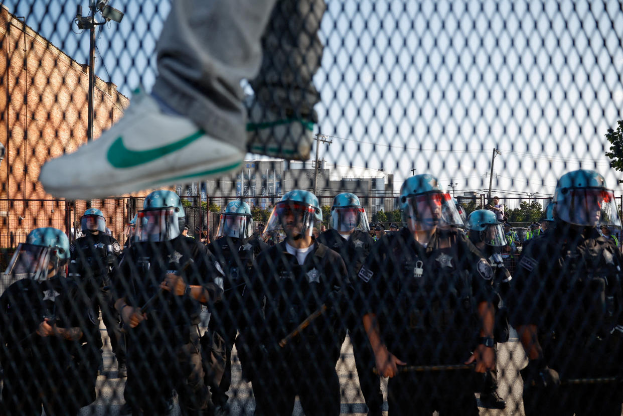 A person's feet dangle as he sits atop a fence in front of riot police outside the Democratic National Convention in Chicago Monday. 