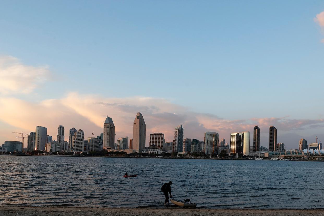 As the sunset illuminates the San Diego skyline, a kayaker launches from a beach, Monday, April 22, 2019, in Coronado, Calif.