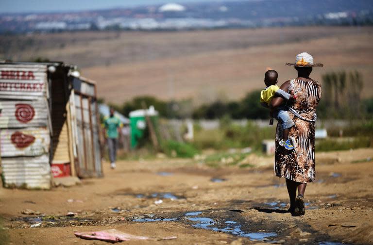 A woman carries her child as she walks alongside a line of shacks in the impoverished township of Diepsloot on the outskirts of Centurion on April 24, 2014