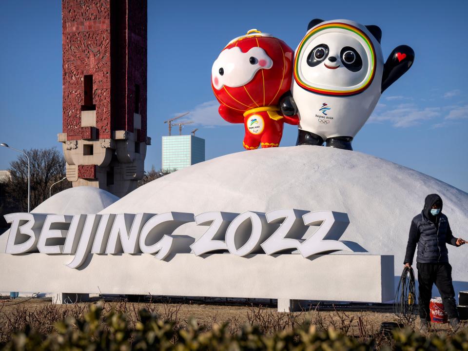 A worker wearing a face mask to help protect against the coronavirus walks past a display of the Winter Paralympic mascot Shuey Rhon Rhon, left, and Winter Olympic mascot Bing Dwen Dwen near the Olympic Green in Beijing, Wednesday, Jan. 12, 2022. Just weeks before hosting the Beijing Winter Olympics, China is battling multiple coronavirus outbreaks in half a dozen cities, with the one closest to the capital driven by the highly transmissible omicron variant.