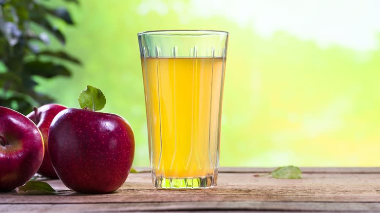 Glass of apple juice with apples off to its left