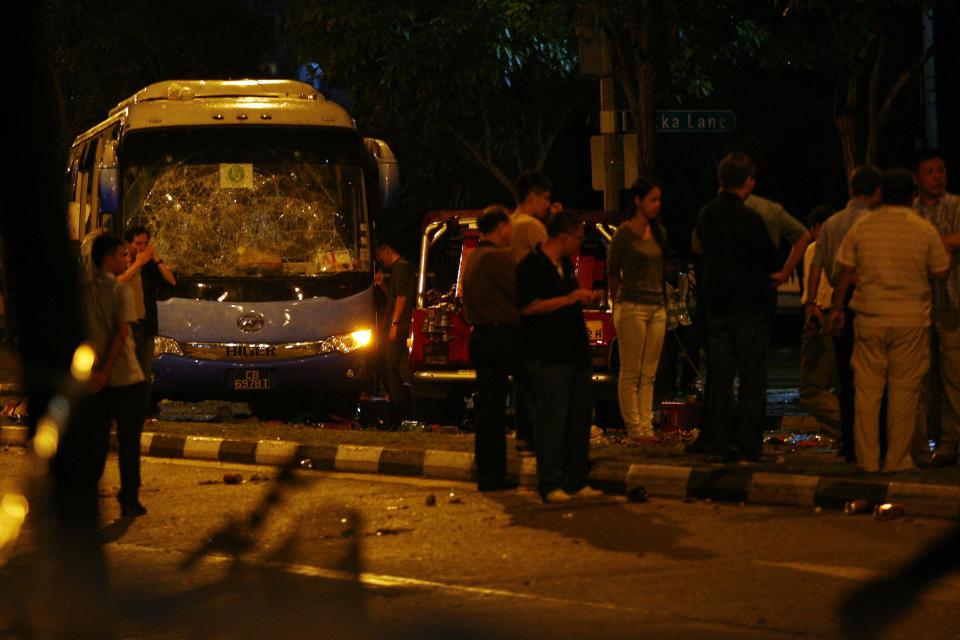 Officials stand around a bus with a smashed windshield following a riot in Singapore's Little India district, December 9, 2013. A crowd set fire to vehicles and clashed with police in the Indian district of Singapore late on Sunday, in a rare outbreak of rioting in the city state. Television footage showed a crowd of people smashing the windscreen of a bus, and at least three police cars being flipped over. The Singapore Police Force said the riot started after a fatal traffic accident in the Little India area. REUTERS/Rob Dawson (SINGAPORE - Tags: CIVIL UNREST)
