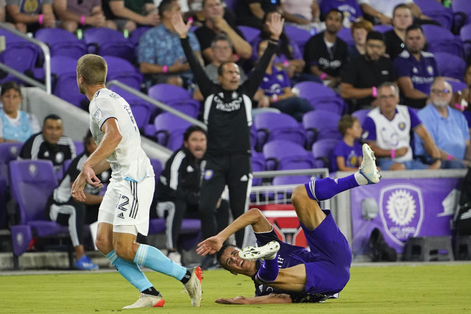 New England Revolution's Justin Rennicks, left, knocks Orlando City's Joao Moutinho to the turf as Orlando City head coach Oscar Pareja, back center, protests to an official during the first half of an MLS soccer match Saturday, Aug. 6, 2022, in Orlando, Fla. (AP Photo/John Raoux)