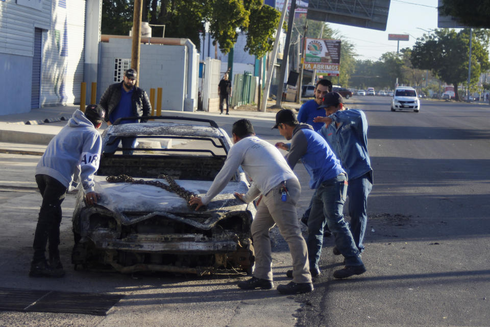 People remove a vehicle from the street that was burned the previous day in Culiacan, Sinaloa state, Mexico, Friday, Jan. 6, 2023. The government operation on Thursday to detain Ovidio Guzman, the son of imprisoned drug lord Joaquin “El Chapo” Guzman, unleashed firefights that killed 10 military personnel and 19 suspected members of the Sinaloa drug cartel, according to authorities. (AP Photo/Martin Urista)