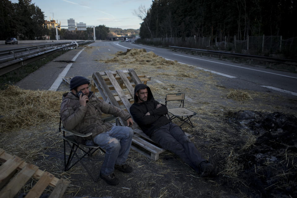 Farmers sit on a highway after spending the night at a barricade in Aix-en-Provence, southern France, Tuesday, Jan. 30, 2024. France's protesting farmers encircle Paris with tractor barricades, vowing a 'siege' over grievances. (AP Photo/Daniel Cole)