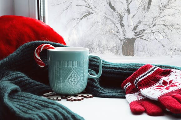 Gloves, scarf, and mug in front of window with snow outside.