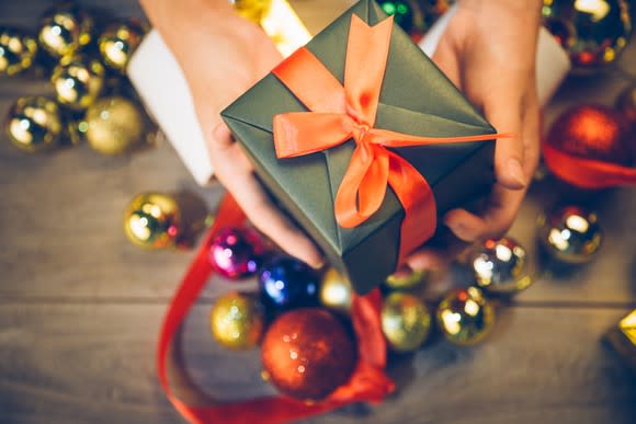 A hand holds out a small gift box.