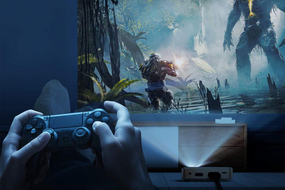 hands playing a video game on a controller, with a jungle scene video game projected on a wall