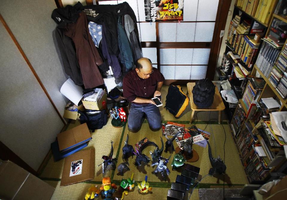 In this Thursday, May 1, 2014 photo, Kazuya Haraguchi, 45, a technician for film reel, responds to a caller in his smartphone with some of his Godzilla collections surrounding him at his apartment in Tokyo. Haraguchi says Hollywood already botched it once with the 1998 remake, directed by Roland Emmerich. And almost everything about the new Godzilla is wrong again, from head to toe - how its arms are limp at its sides, how the scales on its back are too regular, even the shape of its head. (AP Photo/Junji Kurokawa)