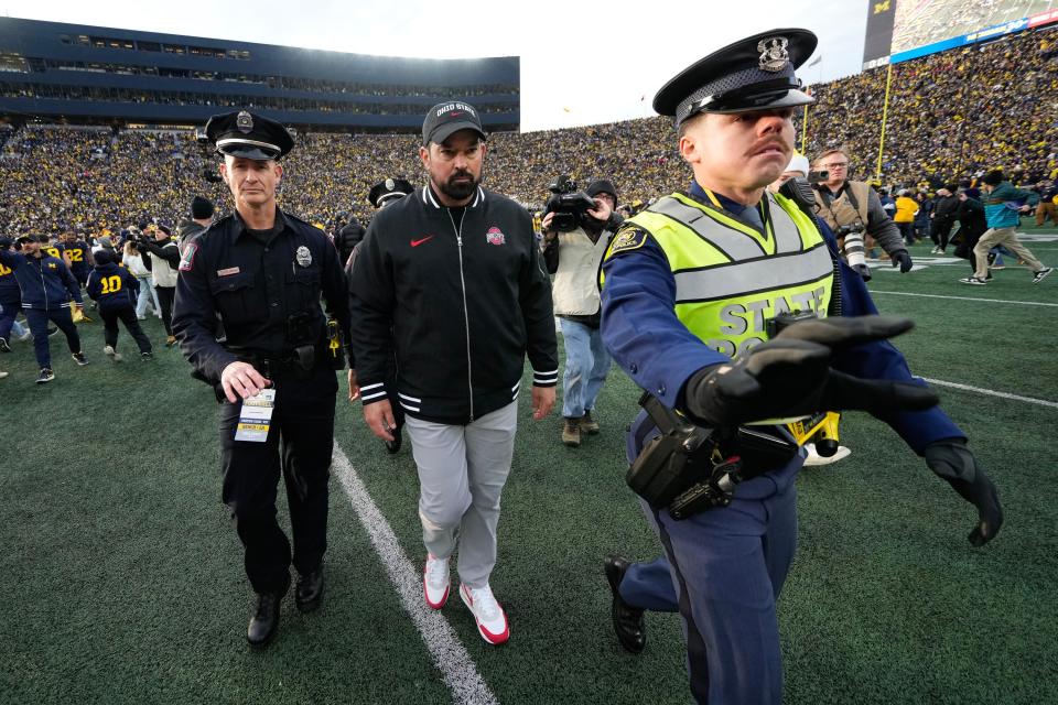 Nov 25, 2023; Ann Arbor, Michigan, USA; As fans rush the field, Ohio State Buckeyes head coach Ryan Day is escorted off the field following the NCAA football game against the Michigan Wolverines at Michigan Stadium. Ohio State lost 30-24.