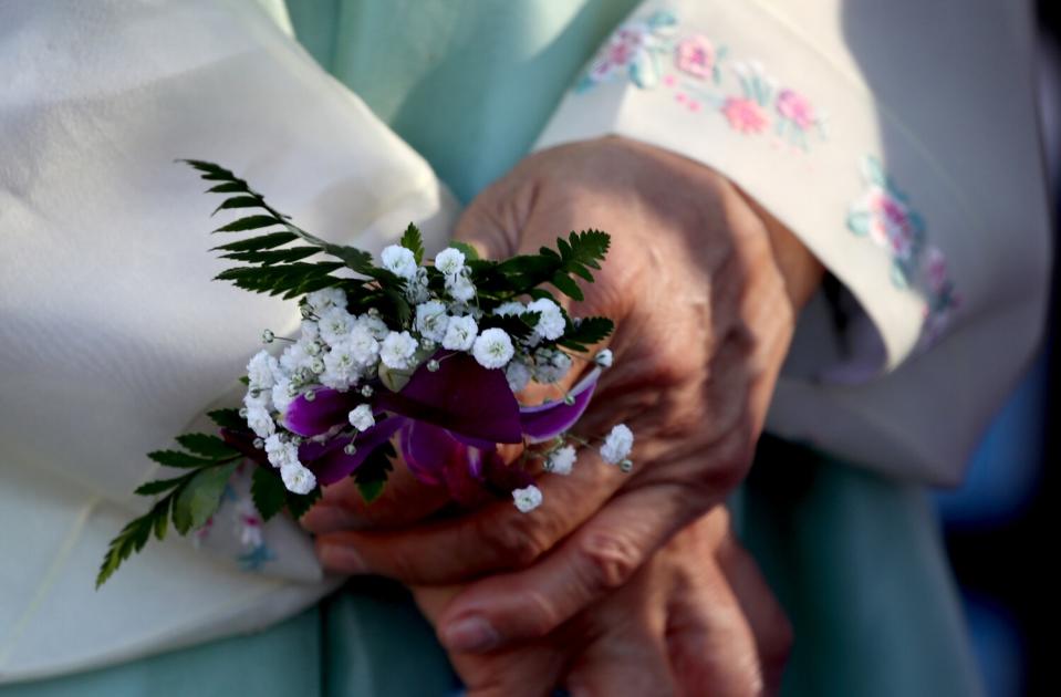 A woman holds flowers and wears a traditional Korean dress during the unveiling of Korean War memorial at Hillcrest Park