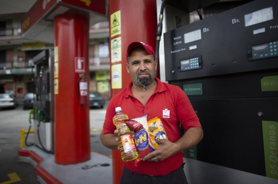 In this Oct. 8, 2019 photo, gas station attendant Leowaldo Sanchez poses with food items he was paid with by motorists: a bottle of cooking oil, a kilogram if rice and a package of corn flour, as he works at the pump in San Antonio de los Altos on the outskirts of Caracas, Venezuela. Bartering at the pump has taken off as hyperinflation makes Venezuela’s paper currency, the bolivar, hard to find and renders some denominations all but worthless, so that nobody will accept them. (AP Photo/Ariana Cubillos)