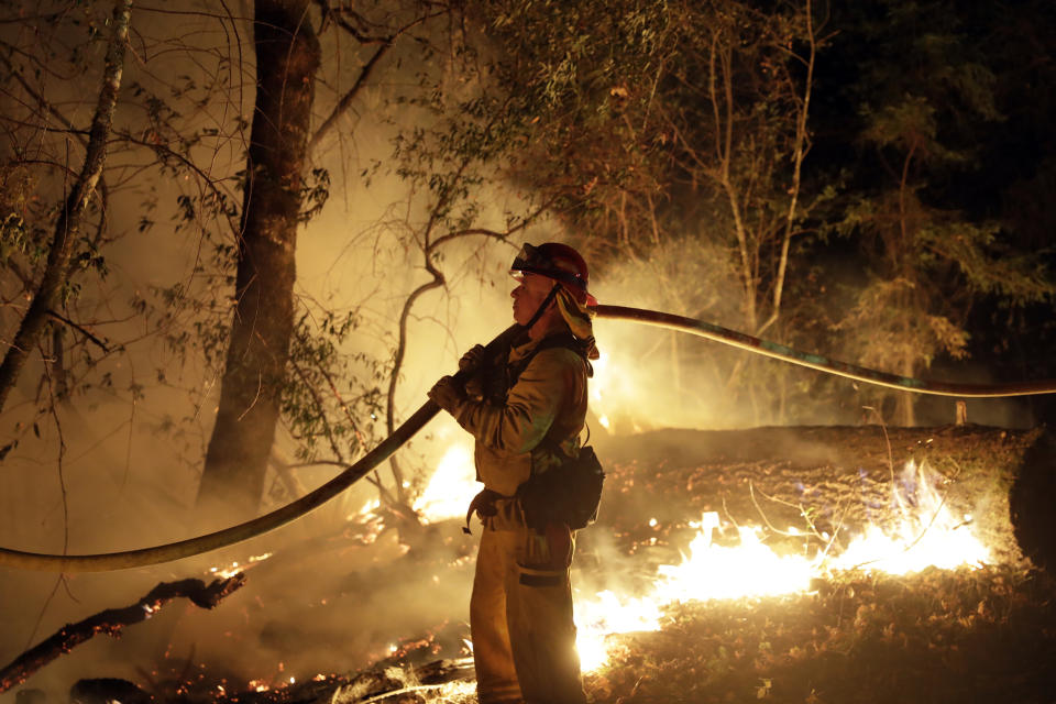 FILE - In this Oct. 14, 2017 file photo, a firefighter holds a water hose while fighting a wildfire in Santa Rosa, Calif. Investigators say the deadly 2017 wildfire that killed 22 people in California's wine country was caused by a private electrical system, not embattled Pacific Gas & Electric Co. The state's firefighting agency said Thursday, Jan. 24, 2019, that the Tubbs Fire started next to a residence. They did not find any violations of state law. (AP Photo/Marcio Jose Sanchez, File)