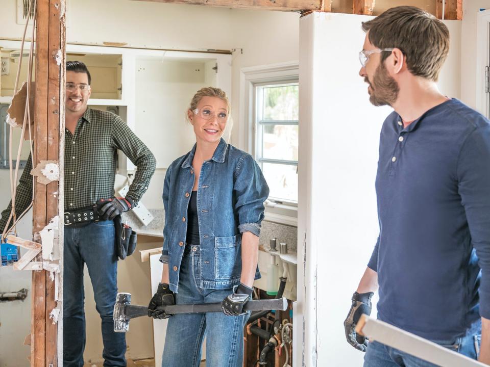 Three people stand in a kitchen being demolished.