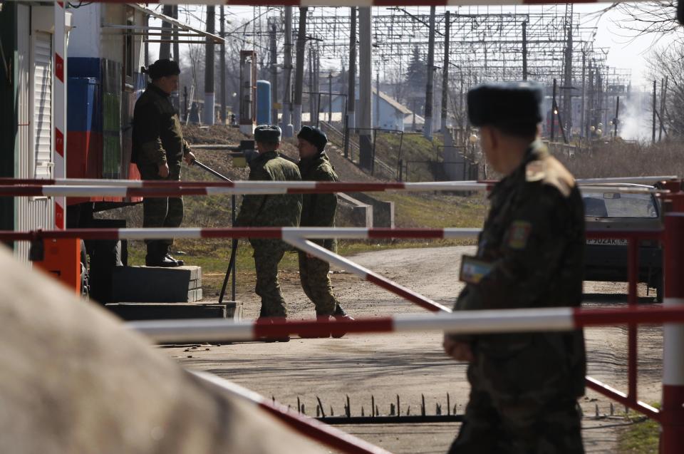 In this photo taken Monday, March 24, 2014, a Ukrainian border guard, right, and Russian border guards, background, stand at the border crossing between Ukraine and Russia in the village of Vyselki, eastern Ukraine. Ever since the 1991 breakup of the Soviet Union, the village of Vyselki has been split between Ukraine and Russia. For years its residents have continued to live together peacefully, doing most of their shopping in one country and paying their electricity bills in another. But after Russia seized the Crimean Peninsula from Ukraine, the Ukrainian villagers fear a further incursion of Russian troops, while the Russians say they would welcome their protection against the new pro-Western government in Kiev. (AP Photo/Sergei Grits)