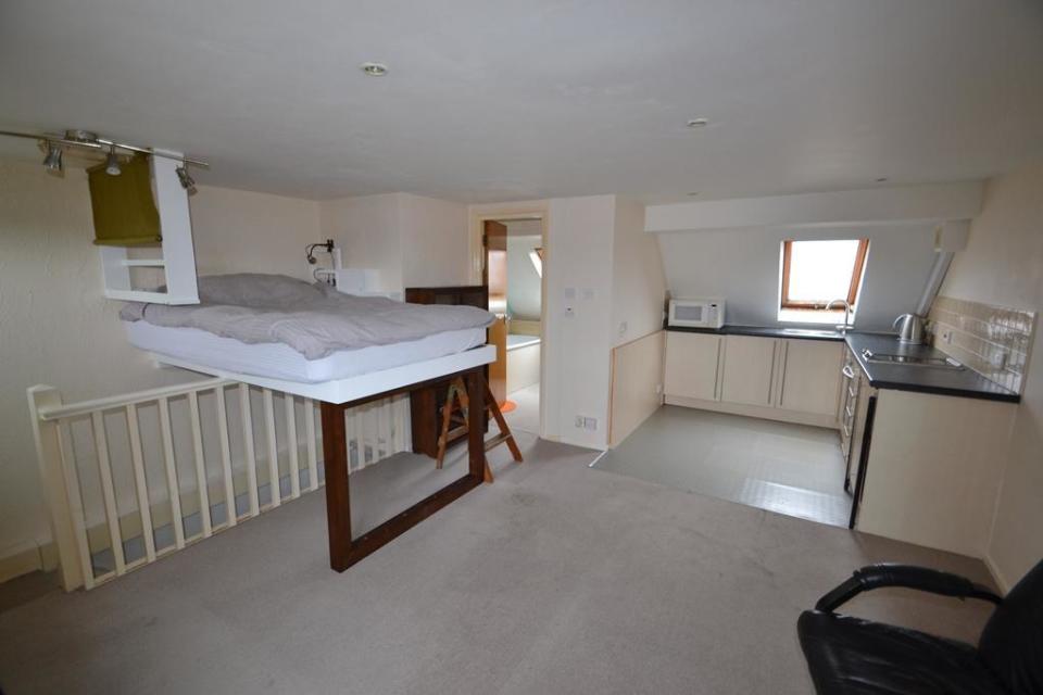 Inside of a studio apartment shows a bed placed over a staircase.