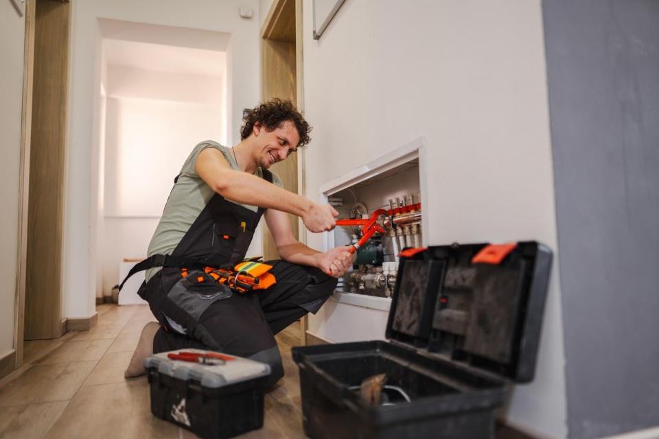 A man in black apron and tool belt tends to a home system with a tool. 