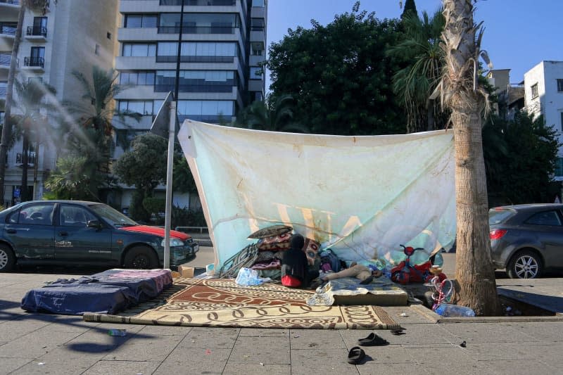 A girl who fled with her family in the southern suburbs of Beirut sits with her sleeping brother in a makeshift tent along Beirut's promenade. At least 1.2 million Lebanese have fled southern Lebanon, the capital's southern suburbs and the Beqaa Valley. Many of them took refuge in the public school, but many had to sleep on the streets. Marwan Naamani/dpa