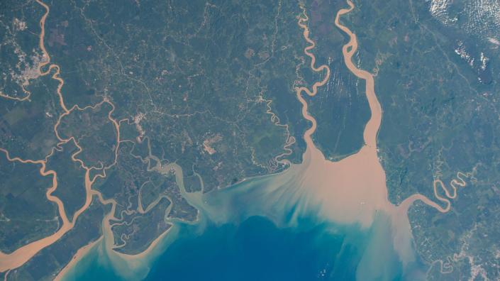 la vue depuis l'espace montre des rivières brunes se jetant dans l'océan bleu à travers un paysage verdoyant