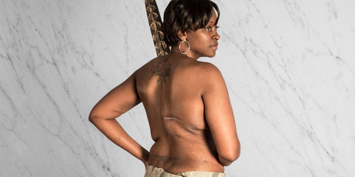 military vet with breast cancer draped in camo poses with a spear