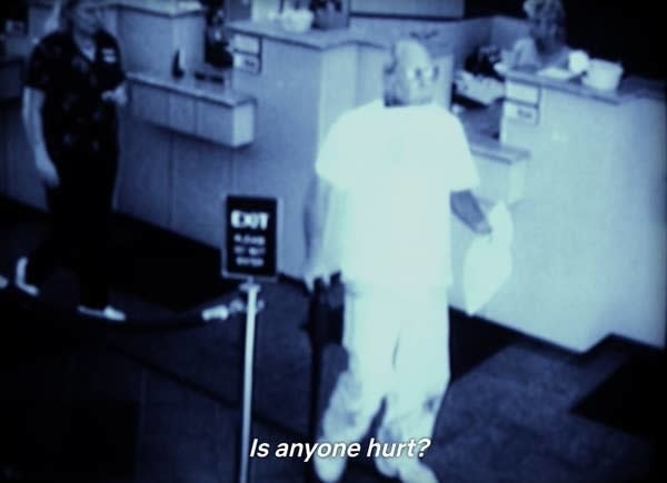 Black and white security footage showing someone at a counter with text "Is anyone hurt?"