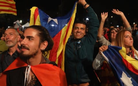  People hold Catalan flags as they listen to Catalan President Carles Puigdemont speak via a televised press conference as they await the result of the Indepenence Referendum at the Placa de Catalunya - Credit: Getty