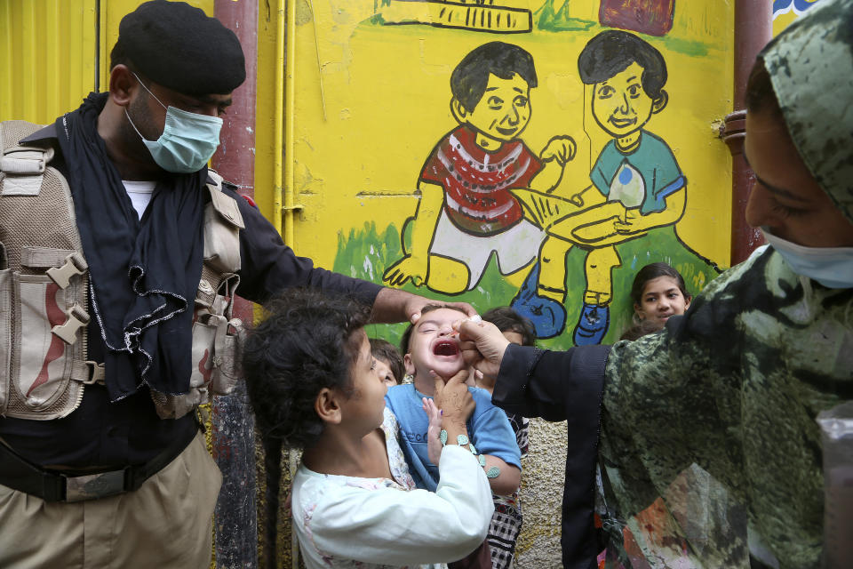 A police officer helps a health worker administer a polio vaccine to a child in Peshawar, Pakistan, Friday, July 30, 2021. The Pakistani government launched an anti-polio vaccination campaign in an effort to eradicate the crippling disease. (AP Photo/Muhammad Sajjad)