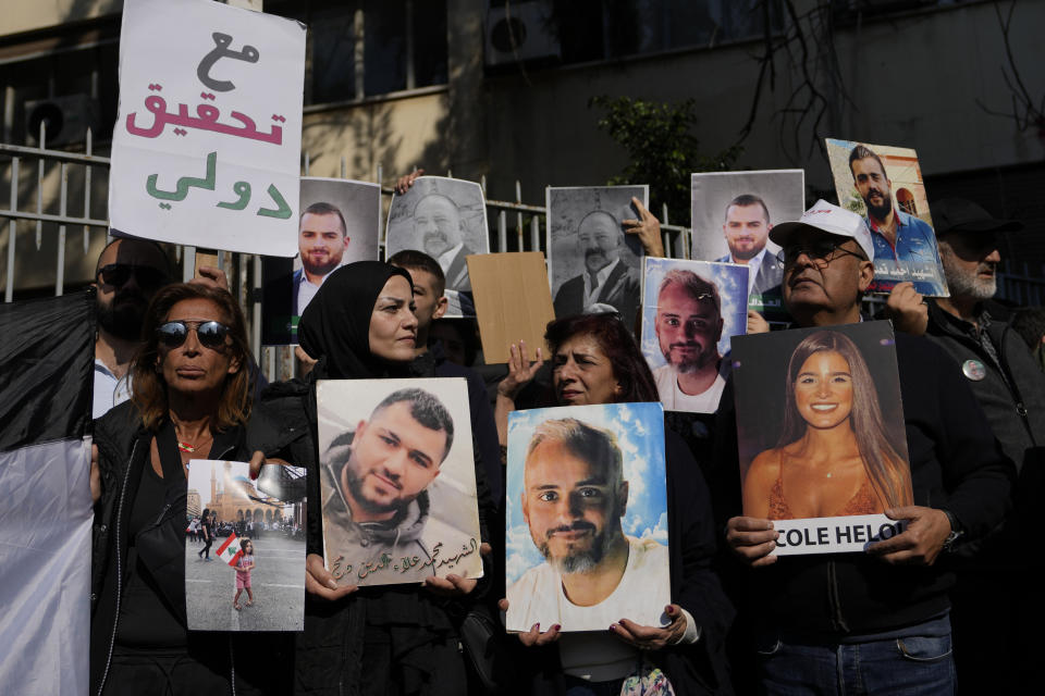 Relatives of victims of the deadly 2020 Beirut port explosion hold portraits of loved ones during a protest in front of the Justice Palace, in Beirut, Lebanon, Thursday, Jan. 26, 2023. Scores of protesters Thursday scuffled with riot police as they tried to break into the Beirut Justice Palace, rejecting an order from Lebanon's judiciary that further crippled the probe into a massive port explosion over two years ago. The placard with Arabic words that reads: "With international investigation." (AP Photo/Hassan Ammar)