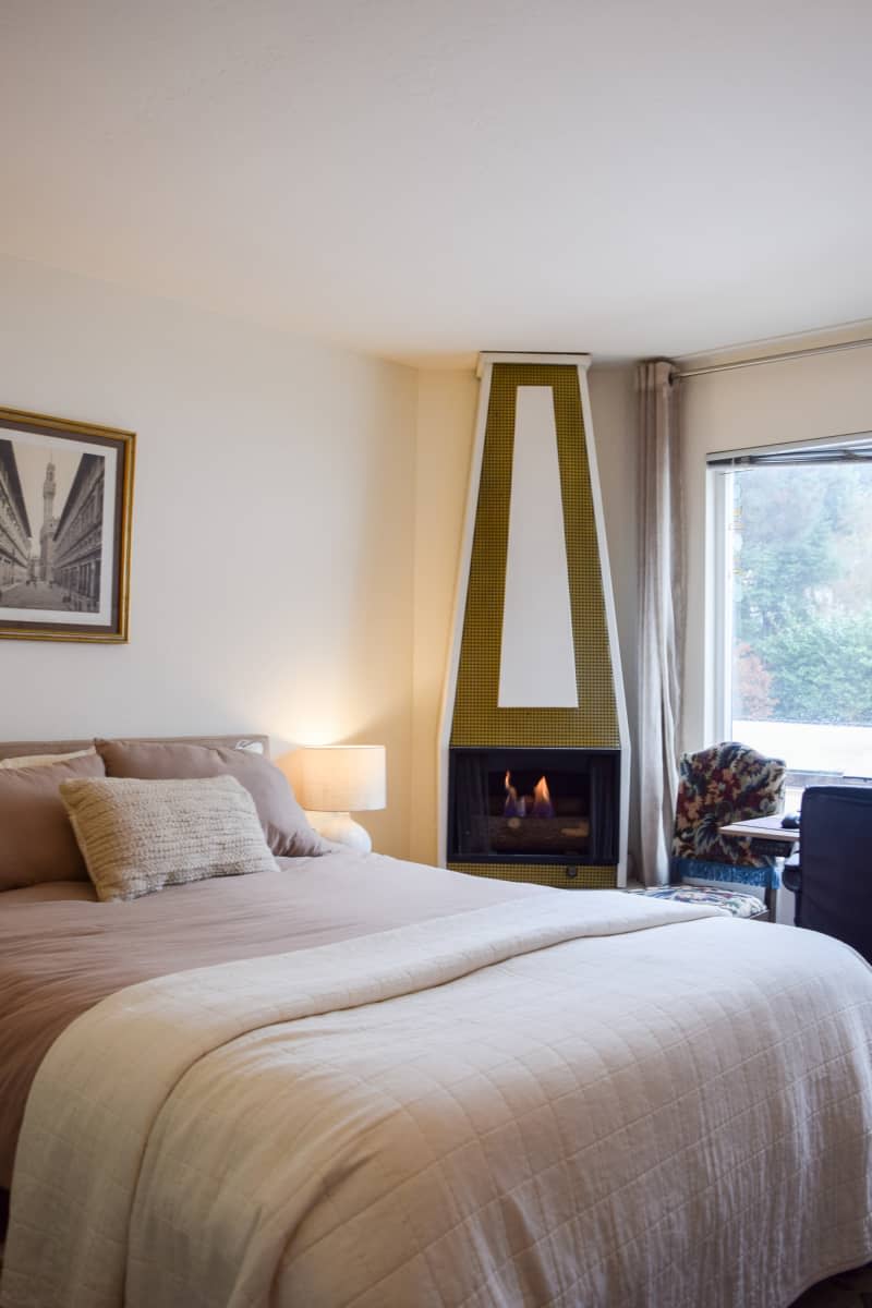 A fireplace next to a bed with derogative pillows