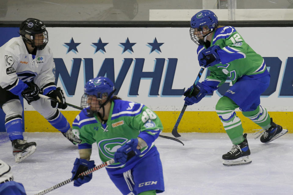 FILE - Connecticut Whale defender Maggie LaGue (12) moves the puck up the ice as Minnesota Whitecaps forward Haley Mack (19) defends during the first period of a semifinal in the NWHL Isobel Cup hockey tournament in Boston, in this Friday, March 26, 2021, file photo. The National Women’s Hockey League made a potentially game-changing decision for the sport in approving to double its salary cap to $300,000 for each of its six teams on Wednesday, April 28, 2021, based on projections it is making strides in achieving financial stability entering its seventh season.(AP Photo/Mary Schwalm, File)