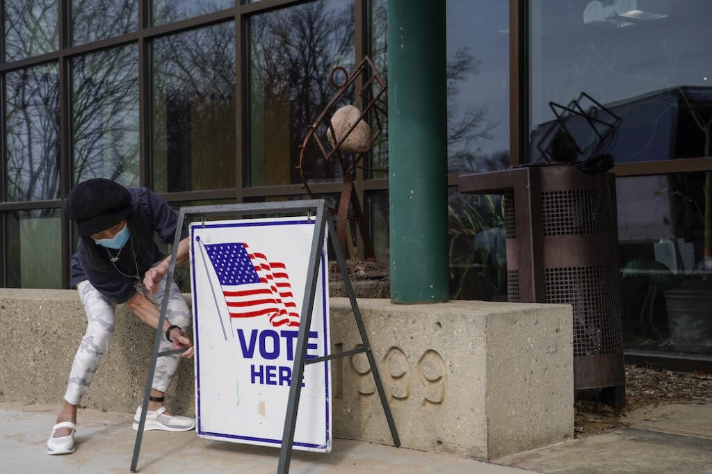 A poll worker places a sign with a flag and the word Vote outside an office.