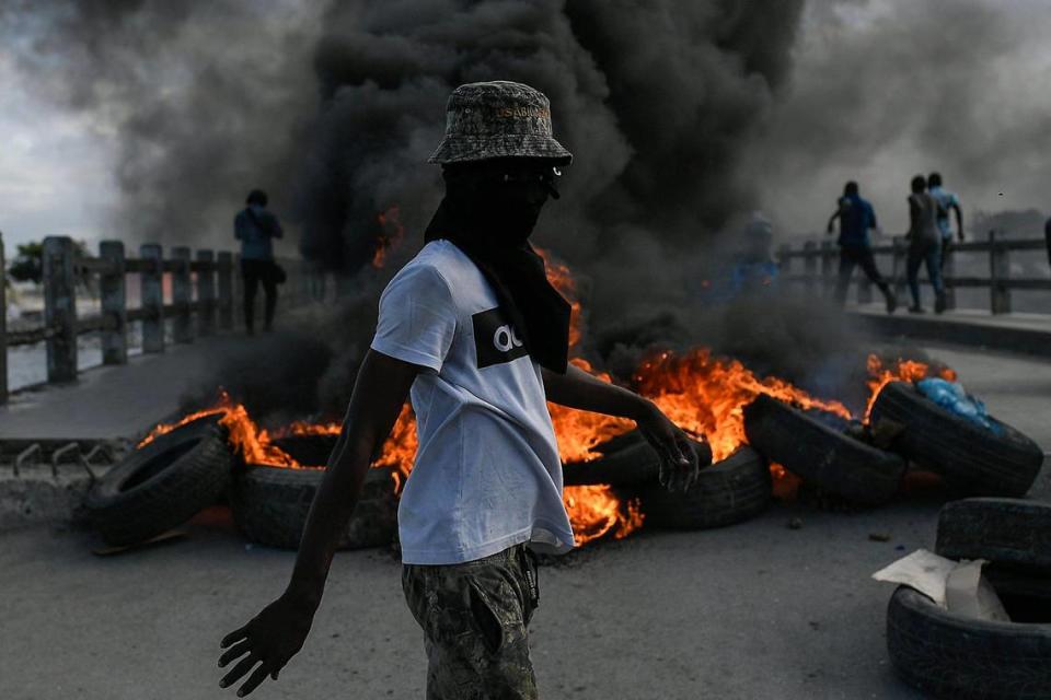 A protester demanding justice for the assassinated President Jovenel Moise stands near a burning barricade in Cap-Haitien, Haiti, Thursday, July 22, 2021. Demonstrations after a memorial service for Moise turned violent on Thursday afternoon with protesters shooting into the air, throwing rocks and overturning heavy concrete barricades next to the seashore as businesses closed and people took cover.