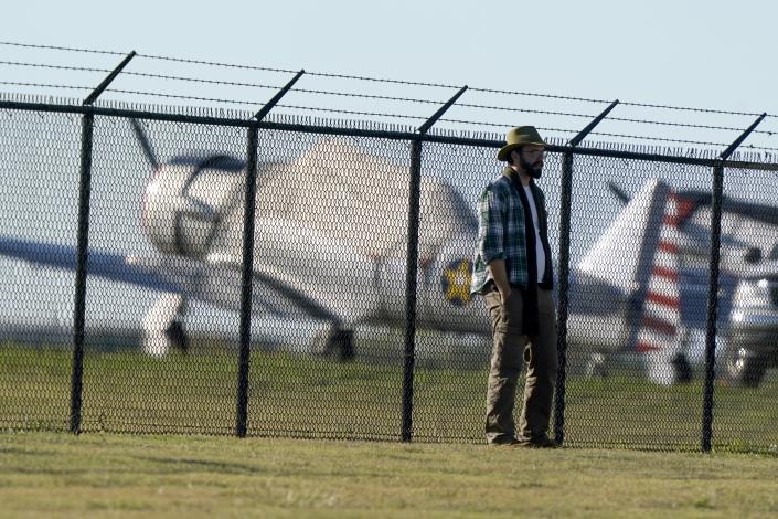 A unidentified person stands by a fence at Dallas Executive Airport where two vintage aircraft crashed during an airshow, Saturday, Nov. 12, 2022. (AP Photo/LM Otero)