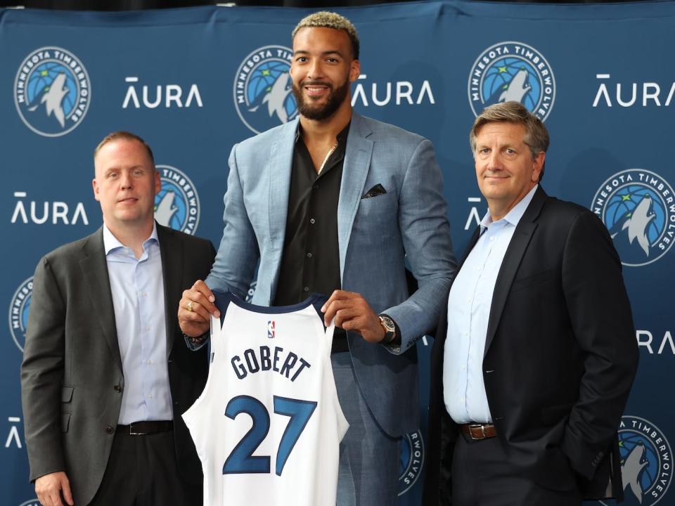 Rudy Gobert holds up a Wolves jersey, surrounded by Tim Connelly and Chris Finch at a press conference.