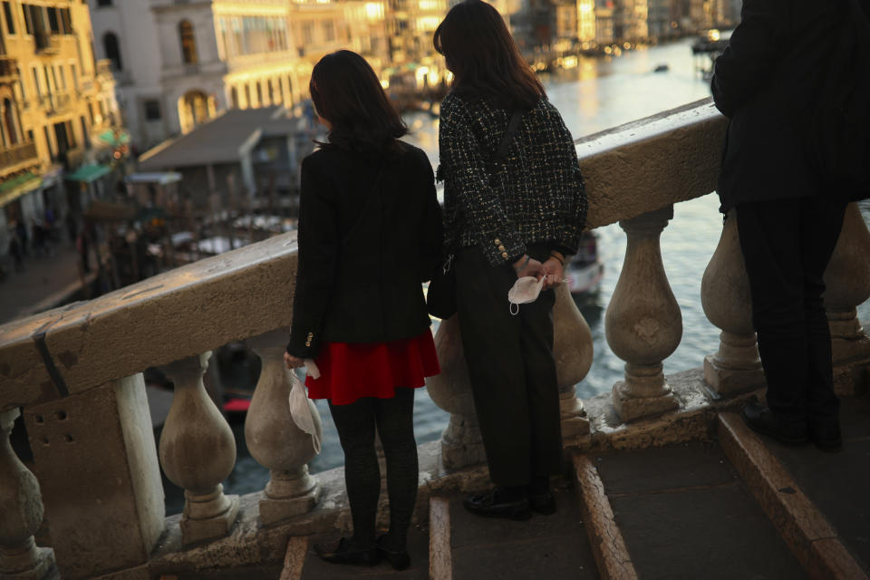 Tourists hold their protective masks as they pose for a photograph at the Rialto bridge in Venice, Italy, Friday, Feb. 28, 2020. Authorities in Italy decided to re-open schools and museums in some of the areas less hard-hit by the coronavirus outbreak in the country which has the most cases outside of Asia, as Italians on Friday yearned for a return to normal life even amid fears that the outbreak could plunge the country's economy into recession. (AP Photo/Francisco Seco)